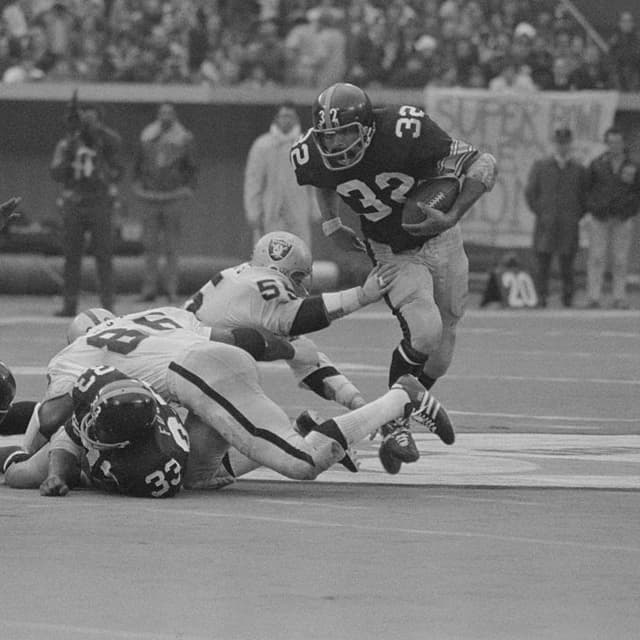 (Original Caption) AFC playoff game- Steeler running back Franco Harris picks up a couple of yards in the 2nd quarter before being pulled down by Oakland Raiders Gerald Irons (86) and Dan Conners (55). Harris has compiled over 1000 yards in rushing this year.