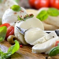 Italian mozzarella cheese snack with cherry tomatoes, basil and olives served on a wooden board with toast bread