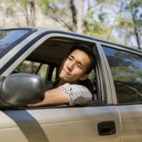 Young man looking away from car window. Male is driving vehicle in countryside. He is on road trip during summer.