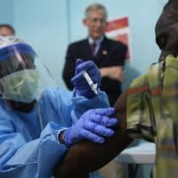 MONROVIA, LIBERIA - FEBRUARY 02:  A nurse administers an injection on the first day of the Ebola vaccine study being conducted at Redemption Hospital, formerly an Ebola holding center, on February 2, 2015 in Monrovia, Liberia. Twelve people were given injections Monday, out of a planned 27,000 people in the Monrovia area. The clinical research study is being conducted jointly by the U.S. National  Institutes of Health (NIH), and the Liberian Ministry of Health. The Ebola epidemic virus has killed at least 3,700 people in Liberia alone, the most of any country, and nearly 9,000 across in West Africa. In background of photo is Dr. Clifford Lane, Clinical Director of the U.S. National Institute for Allergy and Infectious Diseases. (Photo by John Moore/Getty Images)