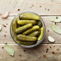 Pickled gherkins or cucumbers in bowl on wooden rustic table from above.