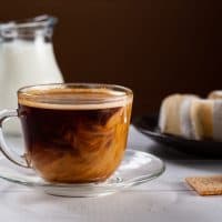 A cup of hot american black coffee with cream poured over. Tasty breackfast with creamy Camembert cheese on natural white wooden table.