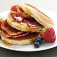 American Pancakes with maple syrup, Bacon, Strawberries and Blueberries on a white plate. Daylight, fresh lighting