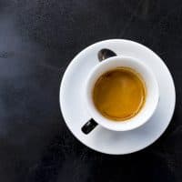 espresso coffee with foam in white cup on black table, copy space, top view