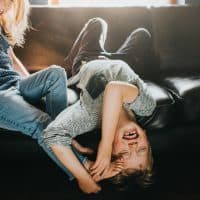 Fun image of a little boy and a little girl playfully messing around on a black leather sofa in a sunny living room. The little girl pokes her bare feet into the little boys face as he giggles and pushes her away. Conceptual with space for copy.