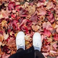 Low section of man with white shoes standing on autumn leaves