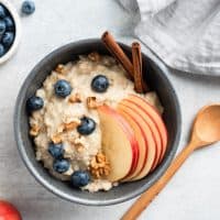 Oatmeal porridge with apple, cinnamon and blueberries in bowl on grey concrete background, top view. Healthy breakfast food for autumn. Comfort food