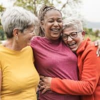 Happy multiracial senior women having fun together outdoor - Elderly generation people hugging each other at park