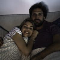 Young couple watching television while relaxing on bed in bedroom