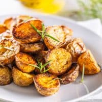 Golden baked potatoes on a white plate with rosemary