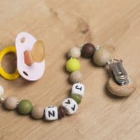 Pink pacifier with handmade playful chain with the baby name on a wooden surface