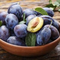 raw plums in a plate on a brown wooden background. place for text