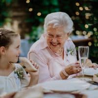 Wedding guests sitting by table, eating and drinking at a reception outside in the backyard.