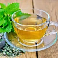 Herbal tea in a glass cup, metal sieve with dry mint leaves, fresh mint leaves on the background of wooden boards