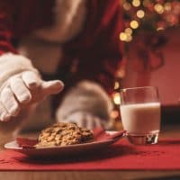 Santa Claus having a delicious snack, he is eating cookies and drinking milk, Christmas and holidays concept