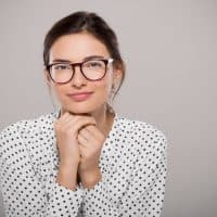 Young woman wearing modern eyeglasses anf thinking isolated on grey background with copy space. Portrait of smiling fashion student wearing big glasses. Proud young businesswoman with spectacles looking at camera.