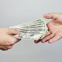 Business closeup of two hands exchanging dollars on grey background.