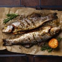 Grilled Fish Sea bass on metal grill grid with lemon and rosemary on dark background