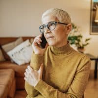 A worried senior woman with short gray hair is talking on the phone