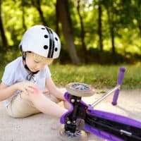 Toddler boy in safety helmet learning to ride scooter. Little child crashing during active outdoors game