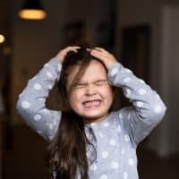 Unhappy small child in bedroom, eyes closed.