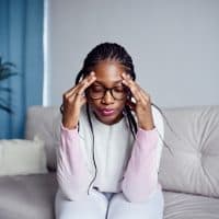 A young woman is sitting on the sofa at home with her head in her hands. The concept of health problems , headache or stress