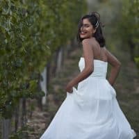 Portrait of smiling young bride wearing wedding dress running while looking back over shoulder in vineyard