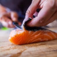 Cette photographie présente en cuisine une personne en train de découper du poisson, notamment du saumon, un pavé.