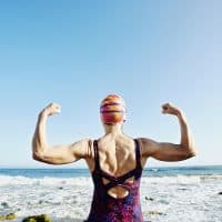 Older Caucasian woman flexing her muscles on beach