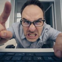 angry hayter writes negative comments on the social network. Negative emotions of a businessman employee in front of a computer. malice and hatred concept. offended nerd reads the message on website.