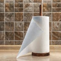 Paper towels on a wooden holder on the table against the background of a tiled wall.