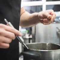 Closeup on chef hands pouring spices to the soup