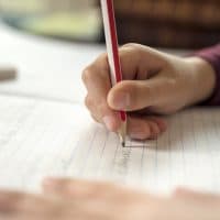 Boy writing in a notepad doing his school work spelling or homework