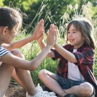 Two little friends playing outside. Enjoying the good weather. Happy in nature. Time together. Spring, summer time. Clapping game.