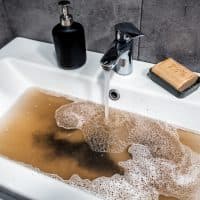?logged sink in bathroom, sink with dirty water, brown soap. Plumbing problems.