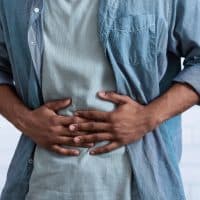 Unrecognizable Black Guy Touching Aching Abdomen Having Painful Stomachache Standing Over Gray Studio Background. African Man Suffering From Stomach Inflammation. Gastritis And Abdomen Pain. Cropped