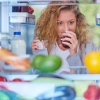 Woman smelling jam in front of fridge full of groceries. Picture taken from the inside of fridge.
