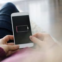 A woman is holding a mobile phone in her hands. On the device screen of the smart phone  visible is an empty battery. The photo was taken over the model's shoulder. I have created the battery icon in adobe illustrator myself. It is intended to look like a generic battery icon.