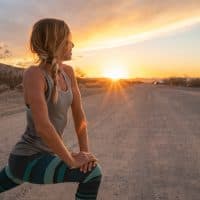 Young woman stretching body after jogging, sunset at the end of the road; female stretches body in nature 
USA