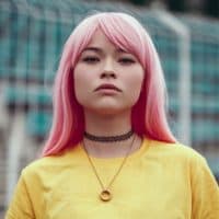 Serious Asian woman with colorful dyed hair and necklace standing by blurred grandstand and looking at camera