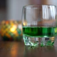 A glass with green absinthe, and a lit candle behind. Short dof, focus on the front side of the glass.