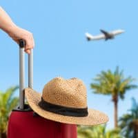 Woman with red suitcase standing on passengers ladder of airplane opposite sea with palm trees. Tourism concept