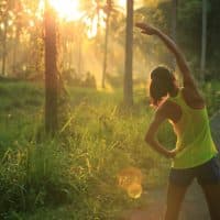 Young female runner warming up before running at morning forest trail