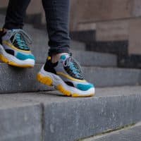 Feet  shod in sneakers multi-colored yellow, white, black and blue down the marble stairs