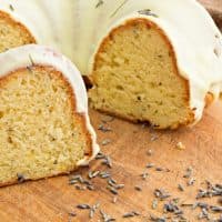 A close up shot of a lemon lavender bundt cake and some lavender blossoms on a wooden cutting board.