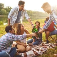 Young people drink, eat and clink glasses at a picnic in a forest near a lake in the summer in the autumn.