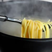 Fork full of cooked spaghetti above a pot of steaming boiling water