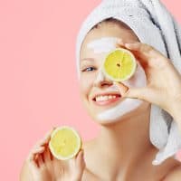 Woman with facial mask holds lemons, over pink background with copy space