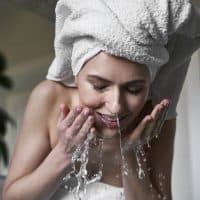 Front view of woman washing face with water in the bathroom