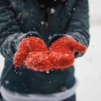 Girl catching snowflakes which are falling on her orange knitted gloves.